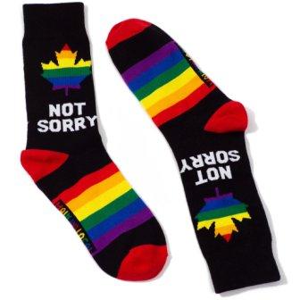 A pair of Not Sorry socks, black with red heel and toe, rainbow stripes on foot, and rainbow maple leaf by cuff. Under the maple leaf, the words "NOT SORRY" in white letters.
