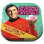 Lid of mints tin. Scottie holding up pink dilithium crystals and smiling. Mint green honeycomb patterned background. Yellow banner across left bottom corner reads "Fresh From The Warp Core." Pink letters at top right read "Pink Peppermint Dilithium Crystals."
