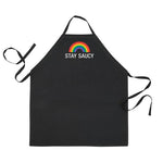 Black apron with rainbow at chest over white text "Stay Saucy."