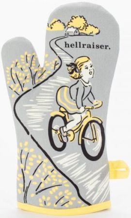 Grey oven mitt with black, white, and yellow illustration of a little blonde girl with hair ribbons, in a skirt, riding a bike down a path away from her rural home. Text above her head reads "hellraiser."